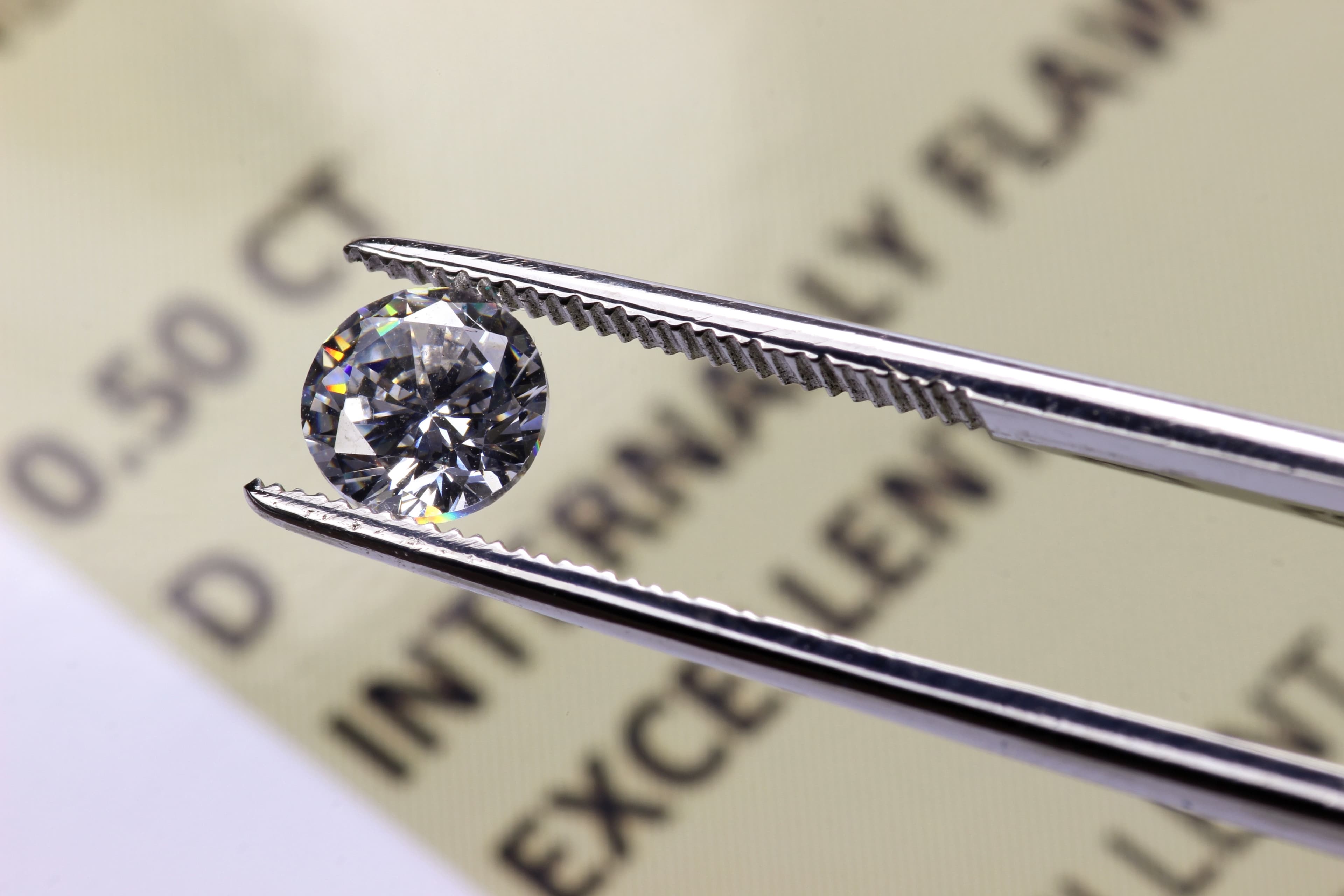 A loose round diamond held in tweezers beside a brass loupe and a diamond grading report card