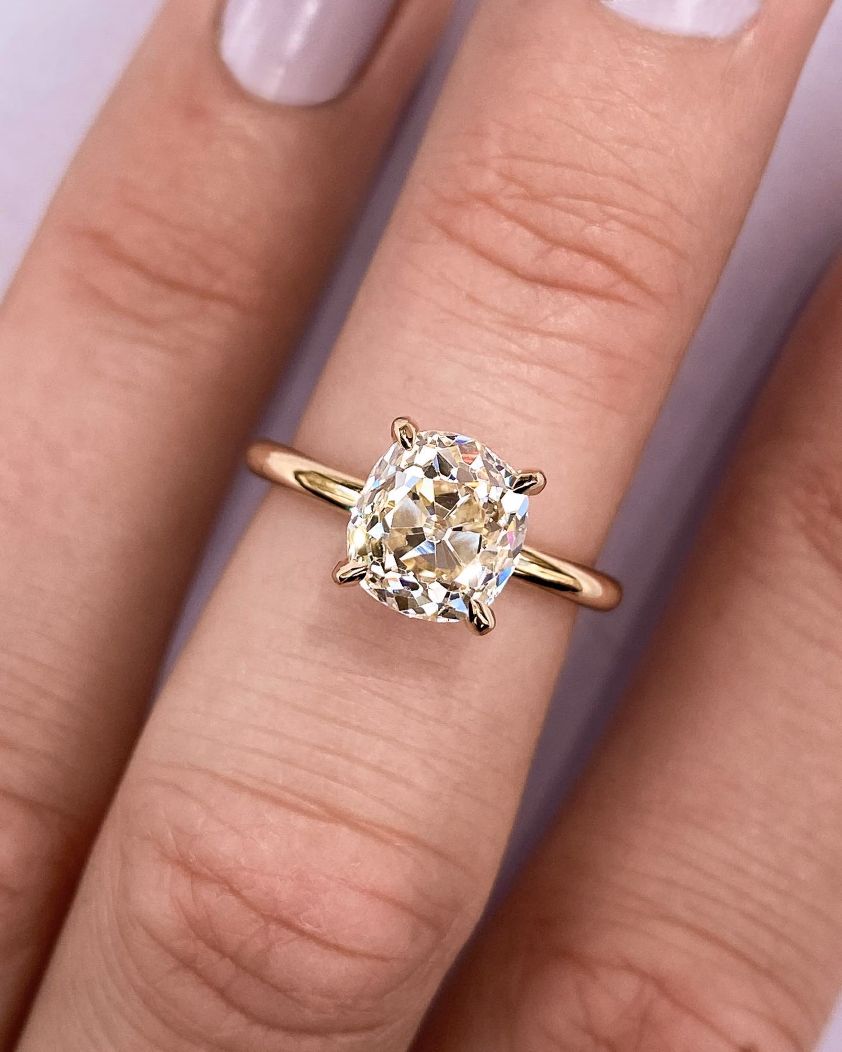 An antique old-mine-cut cushion diamond ring in warm yellow gold glowing under soft light